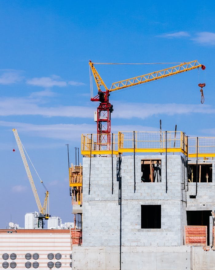 Tower cranes at a construction site working on a high-rise building under a clear blue sky.